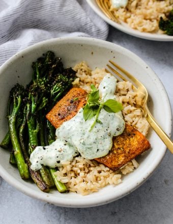 side angle shot of white bowl with broccolini, brown rice, turmeric salmon, parsley yogurt sauce