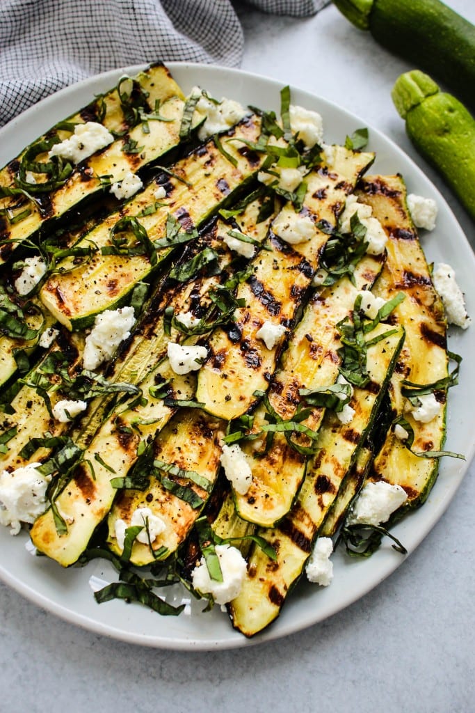 light blue plate with grilled zucchini slices topped with crumbled goat cheese, basil and honey