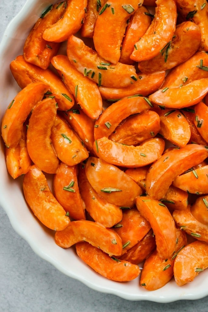 close up sliced apricots and rosemary in white baking dish