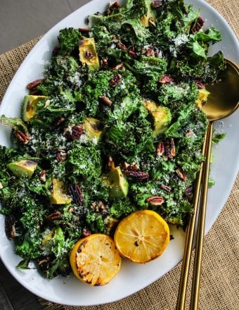 overhead shot white serving plate with grilled kale salad topped with avocado, pecans, parmesan, lemons