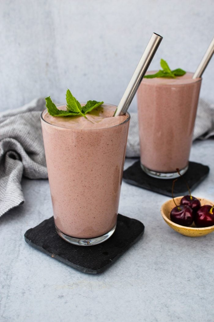 two glasses of cherry yogurt smoothie with mint leaf and straw on top