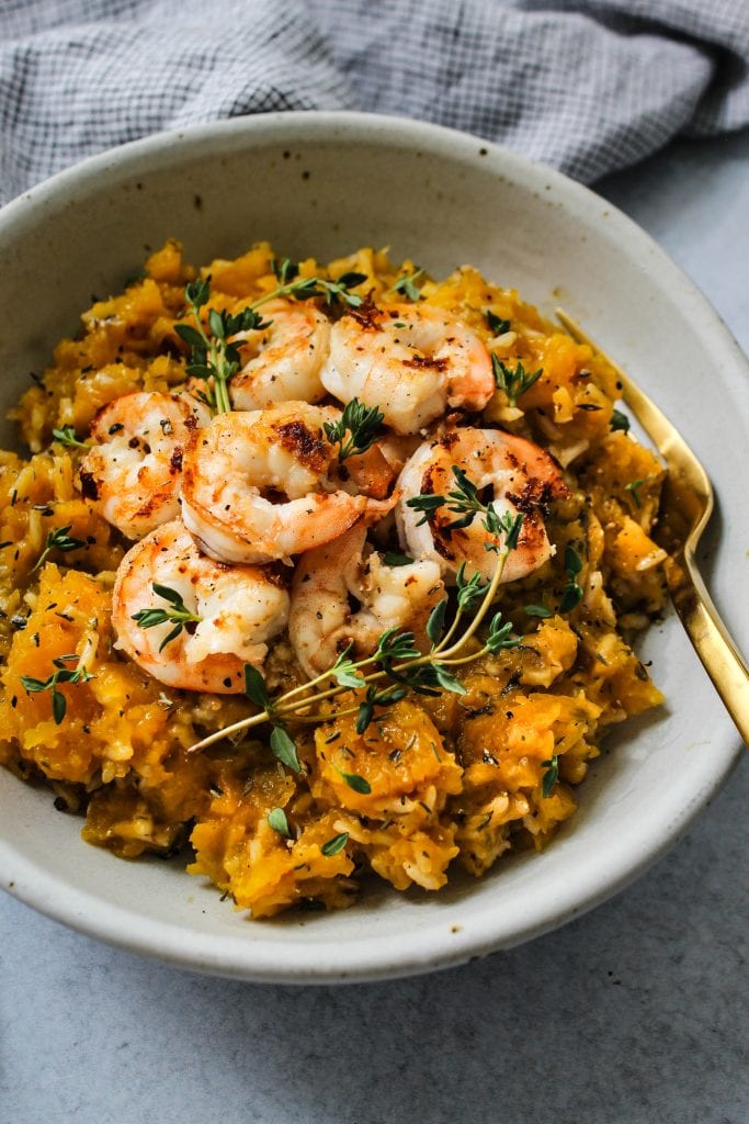 side angle shot of white bowl with butternut squash rice topped with shrimp