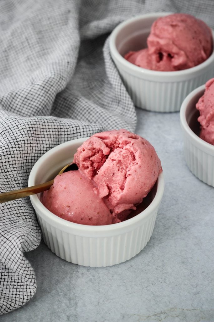 Three white ramekins with scoops of homemade strawberry frozen yogurt inside.