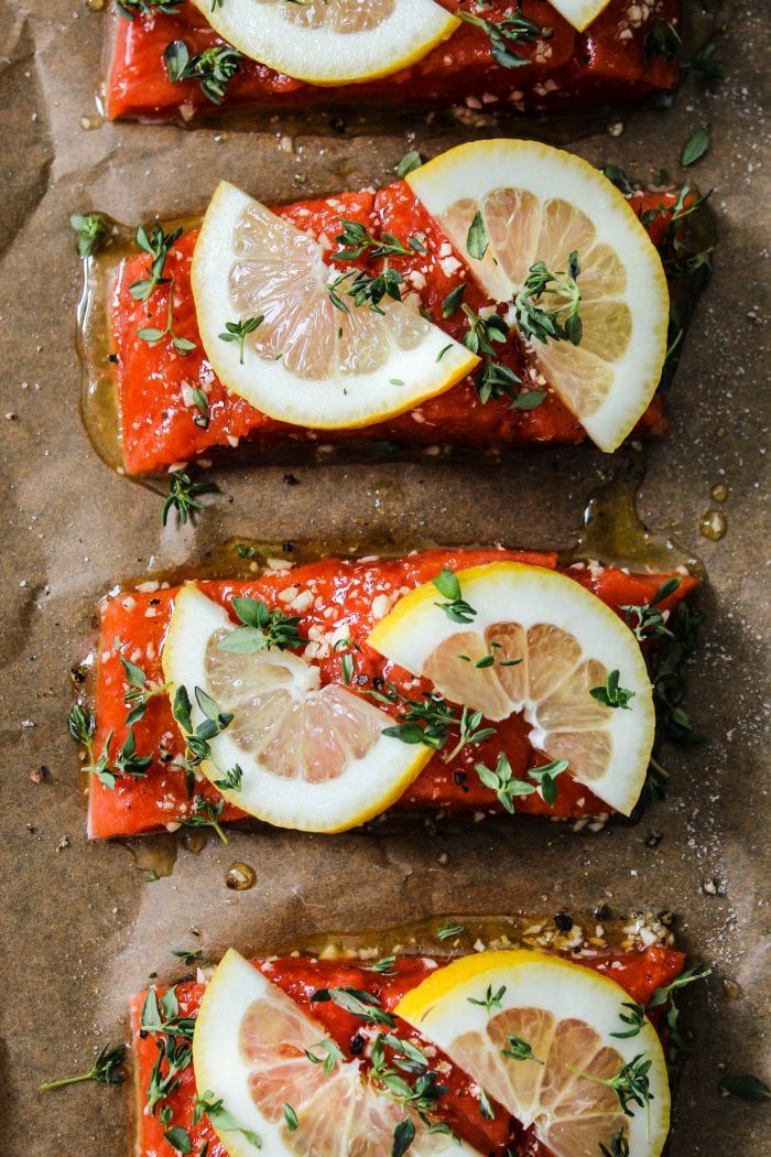 Overhead photo of parchment-lined baking dish with four salmon fillets with lemon and thyme on top.
