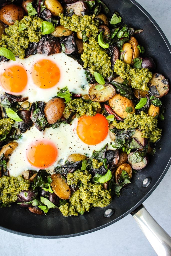 black skillet with pesto potato hash topped with fried eggs