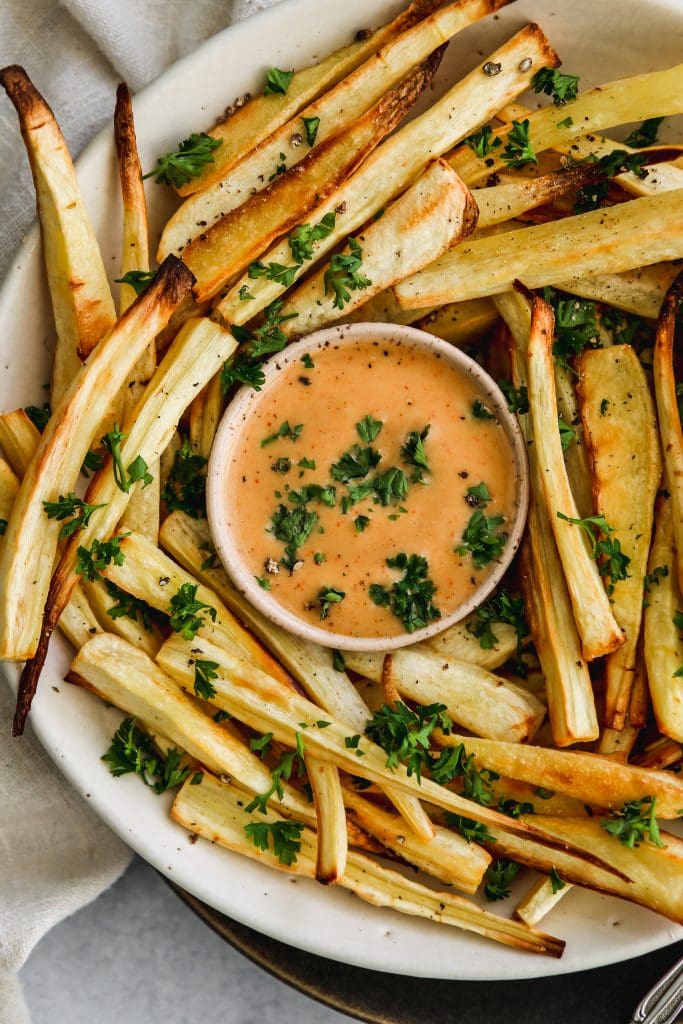 closeup shot of a white bowl of oven-baked parsnip fries and honey mustard sauce