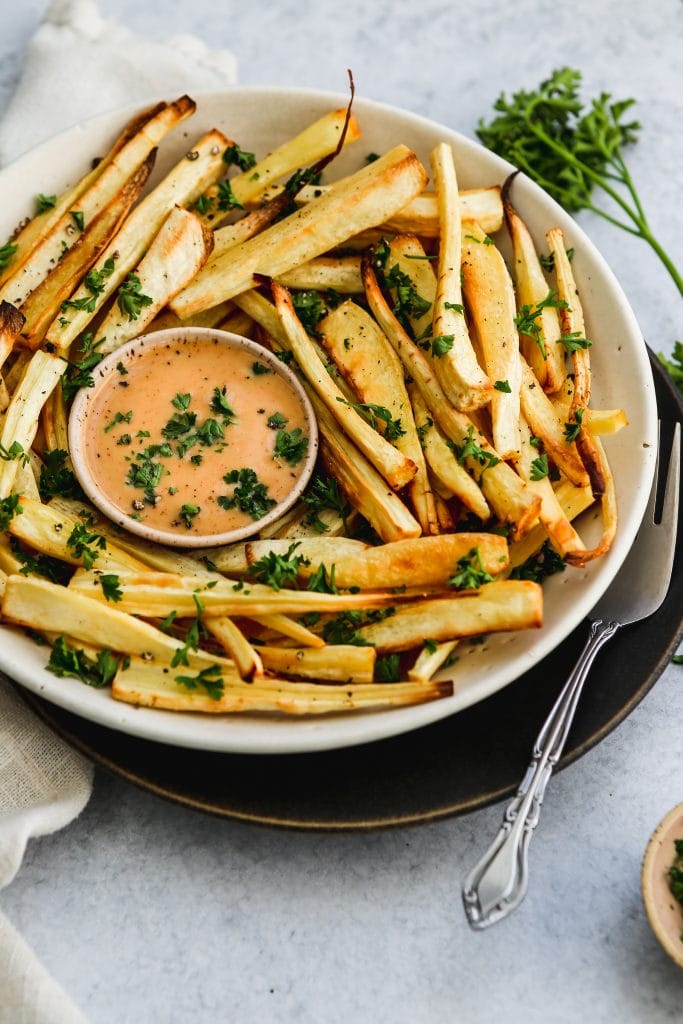 45 degree angle shot of a white bowl of oven-baked parsnip fries and honey mustard sauce