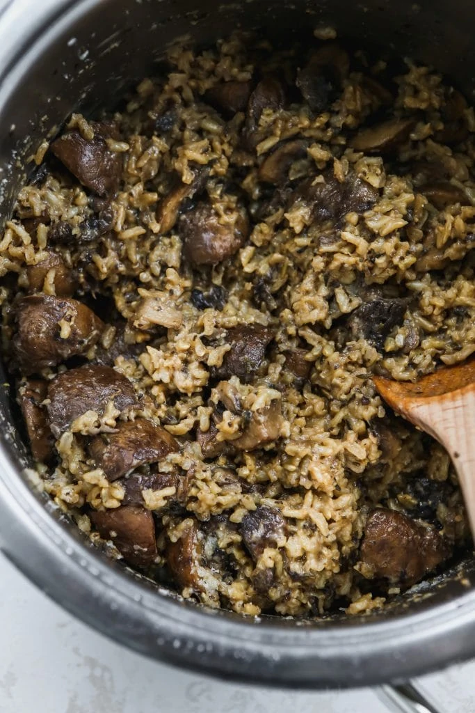 close up photo of large saucepan with a wood spoon stirring brown rice with mushrooms