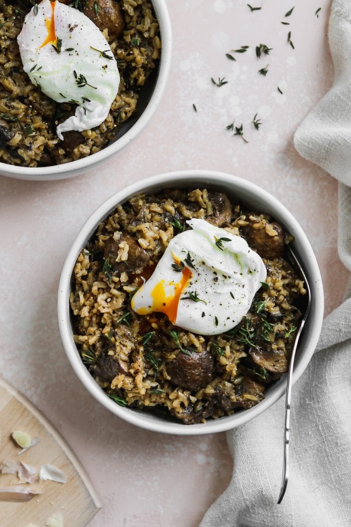 overhead photo of 2 white bowls with miso mushroom rice inside, topped with a poached egg over a light pink backdrop