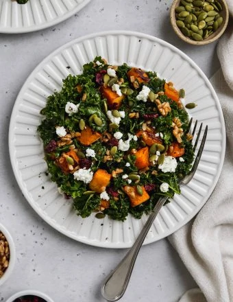 overhead zoomed out photo of kale butternut squash salad with farro and goat cheese on a white plate