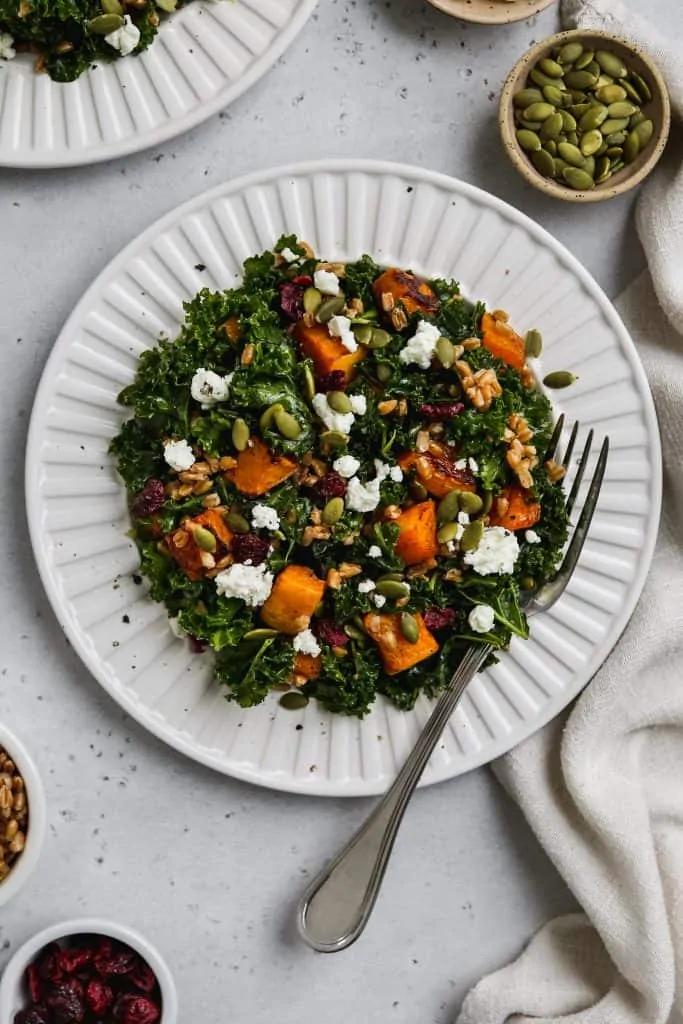 overhead zoomed out photo of kale butternut squash salad with farro and goat cheese on a white plate