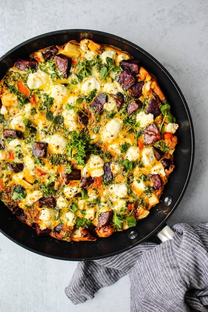 overhead shot of black skillet with a root vegetable frittata, goat cheese, and parsley inside