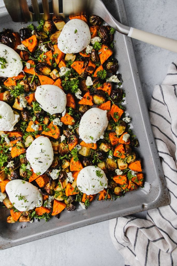 overhead shot of brussels sprouts and sweet potato hash on sheet pan topped with poached eggs