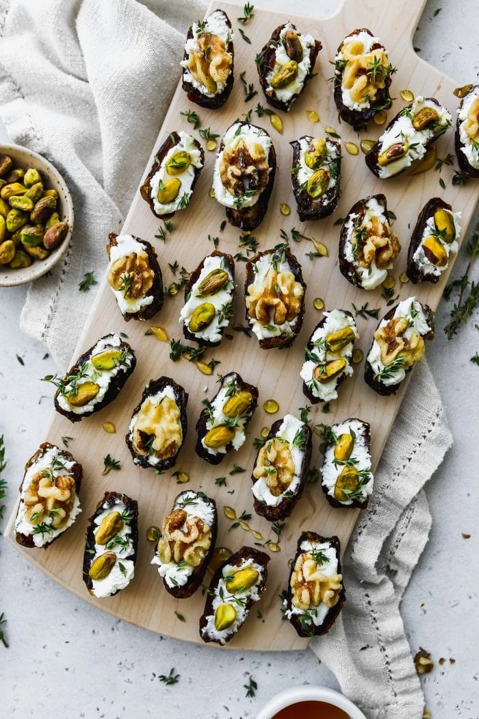 overhead photo of wood cutting board with 25 date halves stuffed with goat cheese and topped with walnuts, pistachios, honey, and thyme