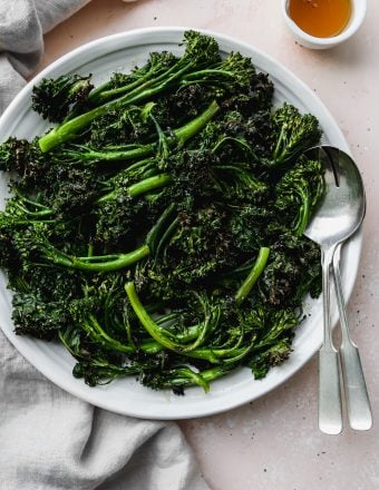 overhead photo of roasted broccolini and kale on a white serving platter with small bowl of honey and silver serving utensils