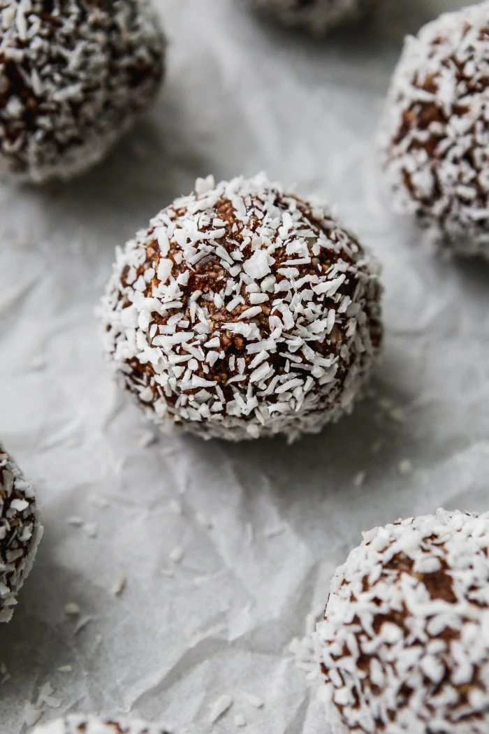 close up photo of coconut date balls on a white piece of parchment paper