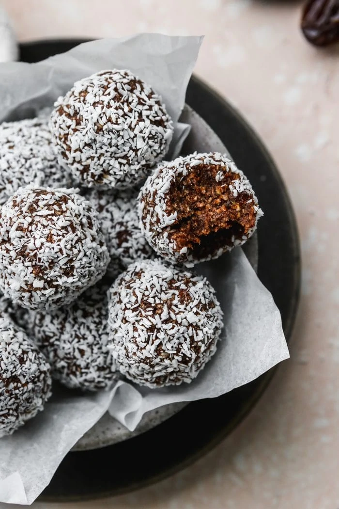 closeup photo of a bowl of healthy chocolate coconut date balls, with one ball having a bite out of it