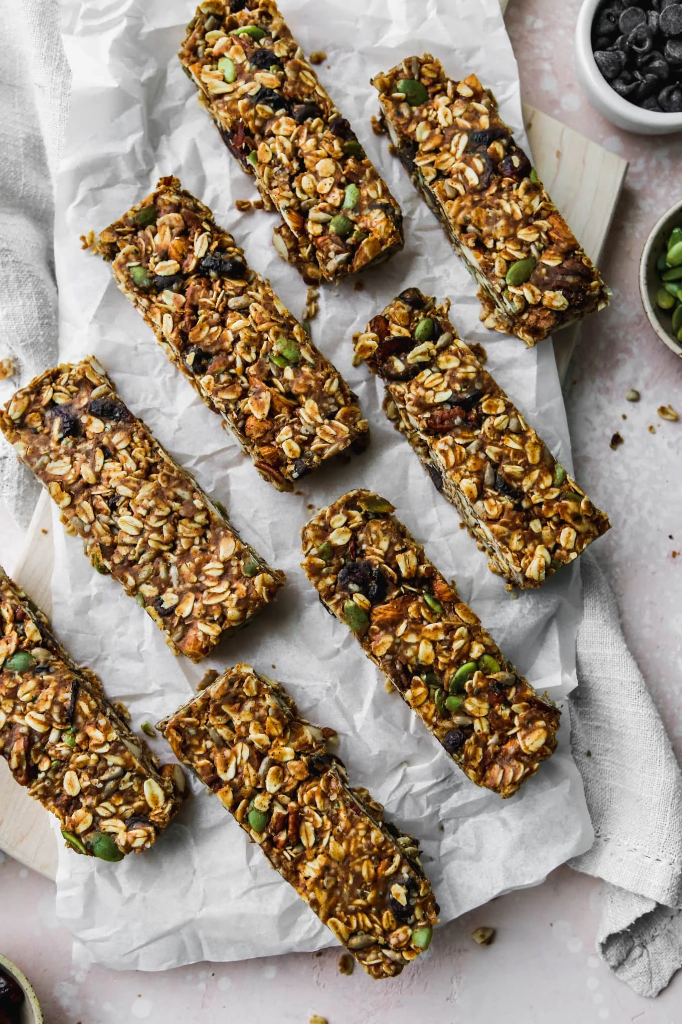 overhead photo of 8 homemade no-bake trail mix granola bars on a wood cutting board with white parchment on top