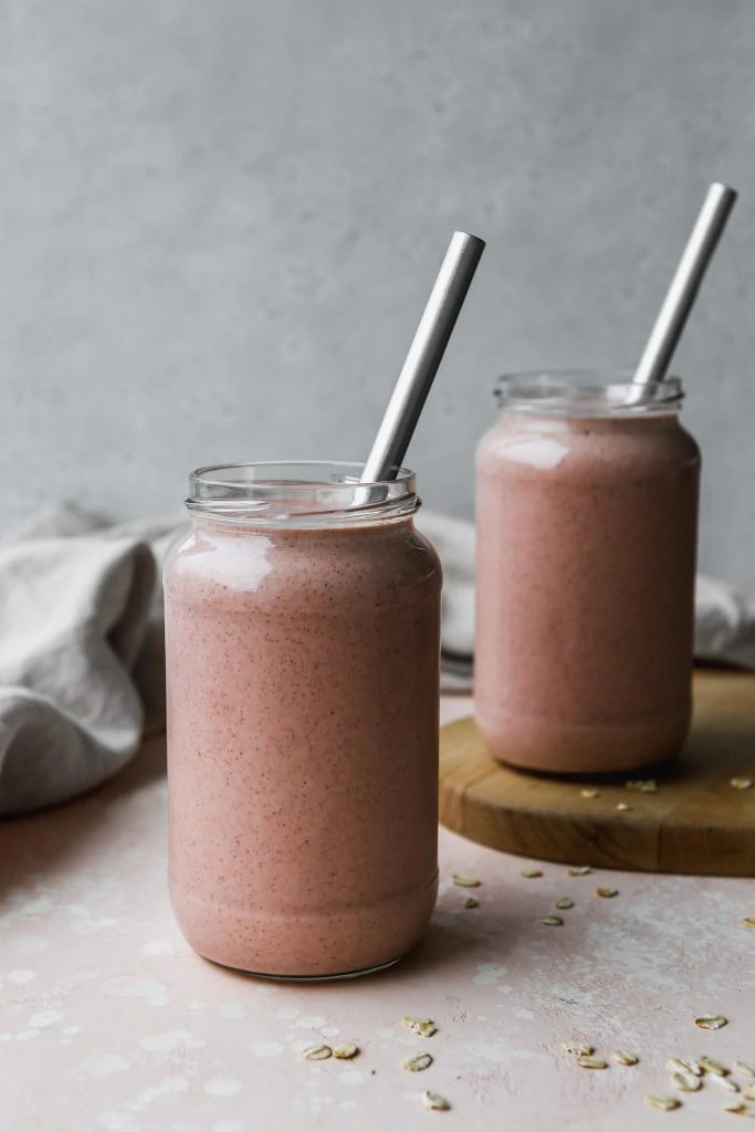 straight on photo of two glass jars filled with strawberry oatmeal smoothie and metal straws