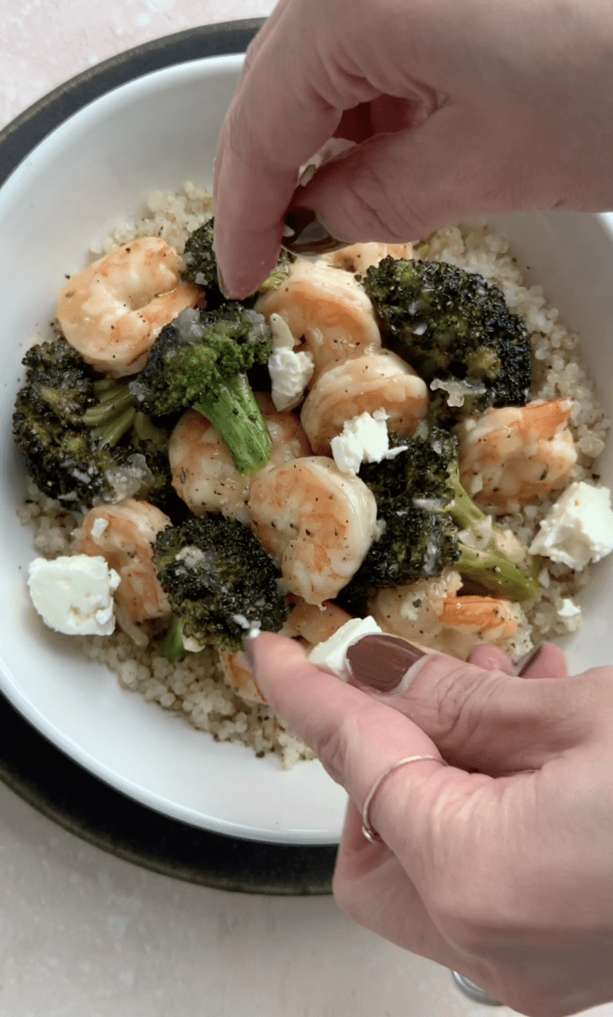 Adding crumbled feta cheese to shrimp and broccoli bowl.