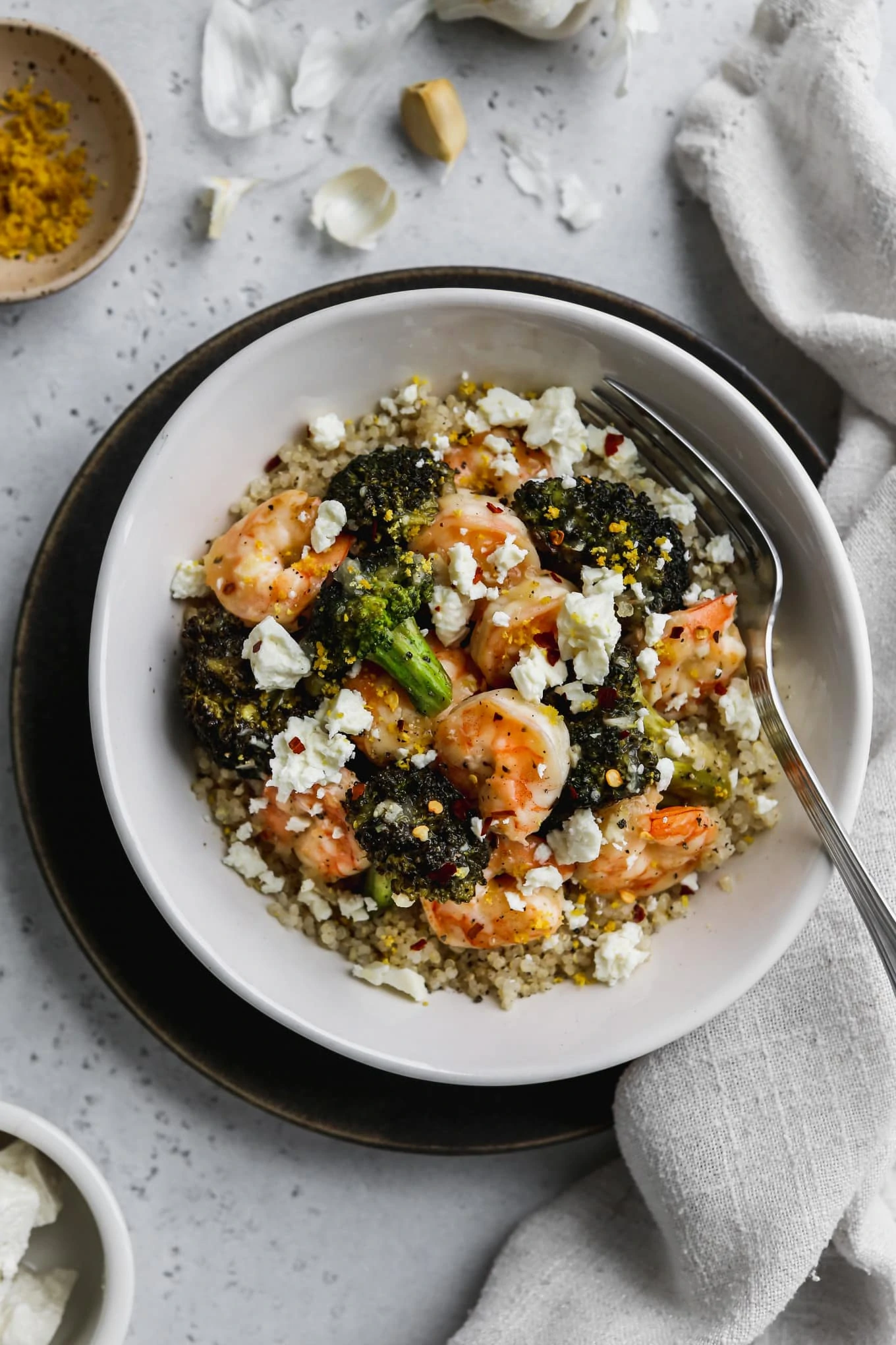 Overhead photo of white bowl filled with quinoa, sautéed shrimp, broccoli, feta, and lemon zest.
