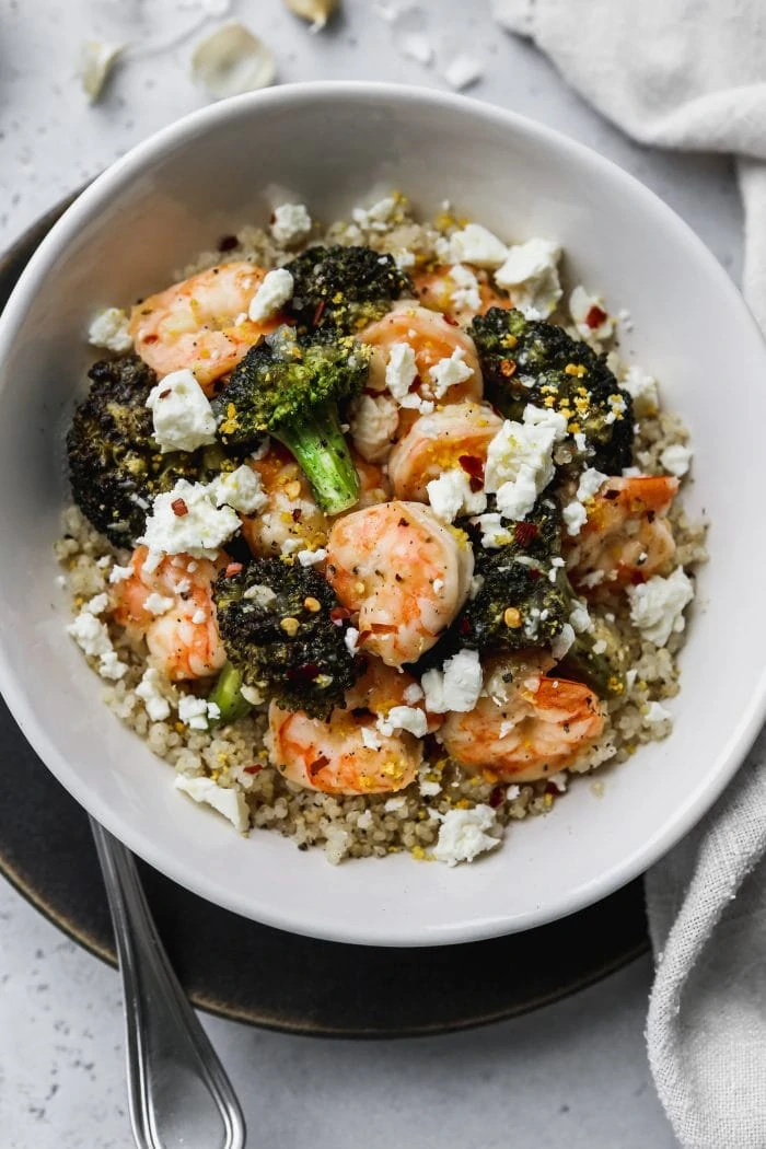 Closeup photo of white bowl filled with quinoa, sautéed shrimp, broccoli, feta, and lemon zest.