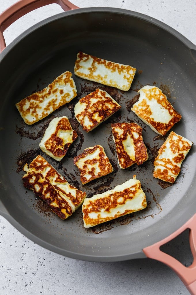 Overhead photo of fried halloumi slices on a frying pan.