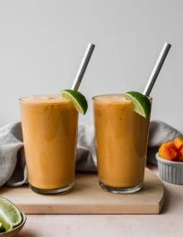 Straight-on shot of two glasses filled with papaya banana coconut and lime smoothie.