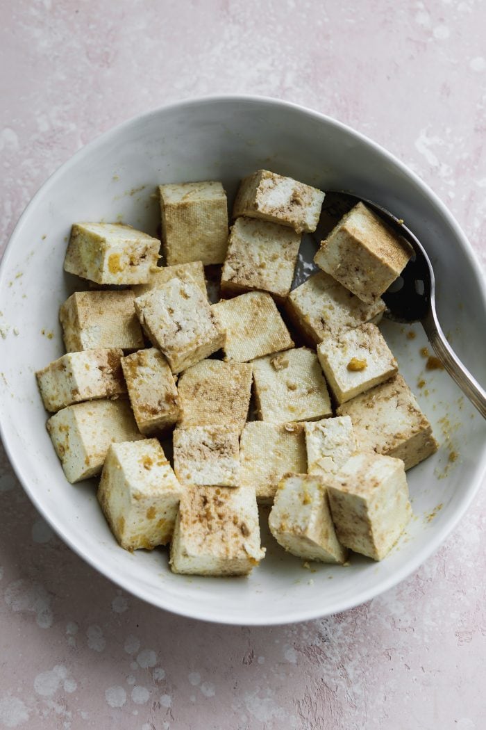 Overhead photo of a white bowl filled with cubes of uncooked tofu.