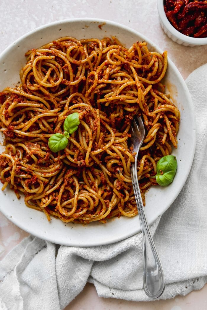 Overhead photo of a white bowl filled with red pesto spaghetti.