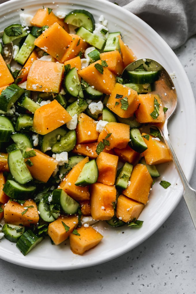 Cantaloupe cucumber feta and mint salad tossed together on a white serving plate.