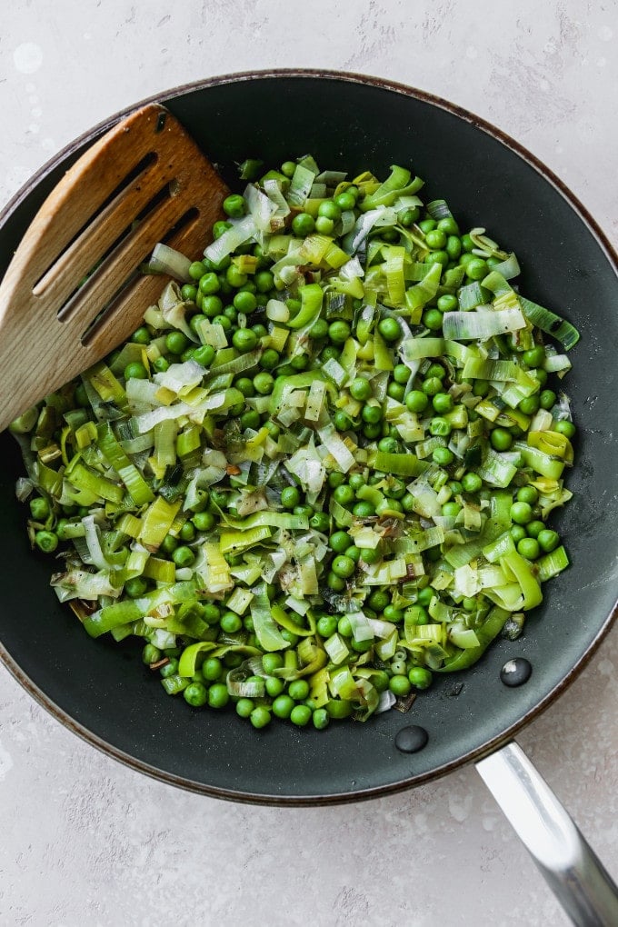 Overhead photo of a frying pan filled with sliced leeks, green onions, and peas.