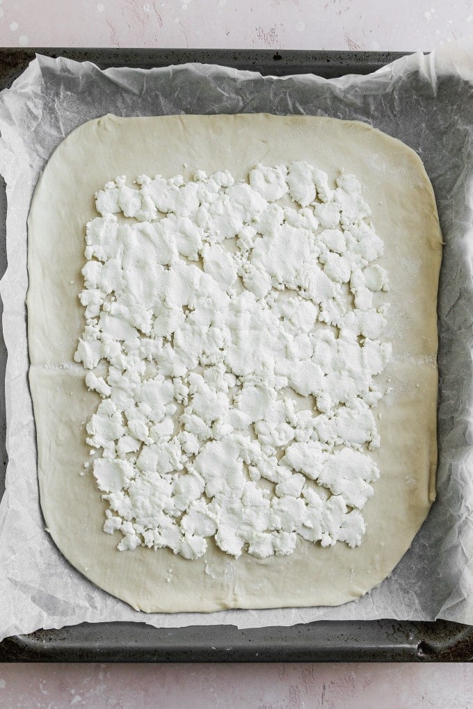 Overhead photo of puffed pastry topped with goat cheese on a parchment-lined baking sheet.