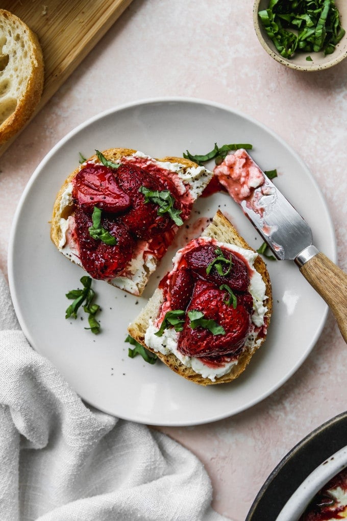 Overhead photo of two slices of toast topped with whipped feta, roasted strawberries, and basil on a small white plate.