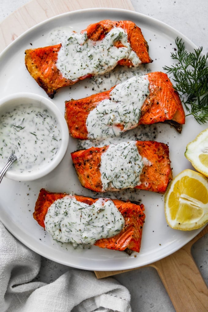 Overhead photo of 4 pieces of grilled salmon topped with yogurt sauce on top of a white plate.