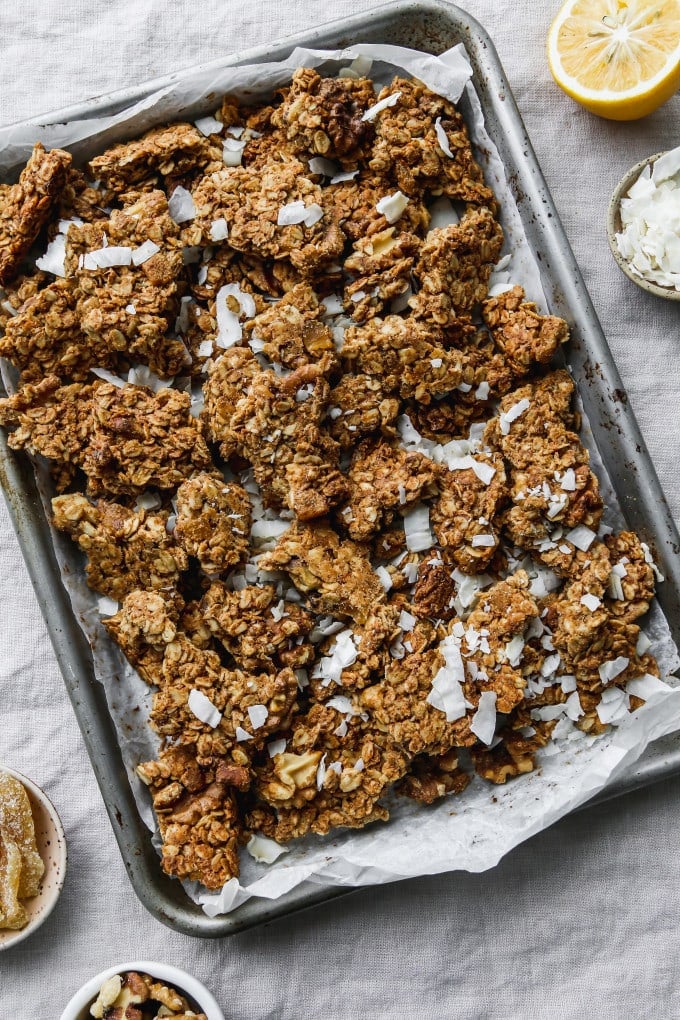 Overhead photo of lemon ginger coconut granola chunks on a parchment-lined baking sheet.