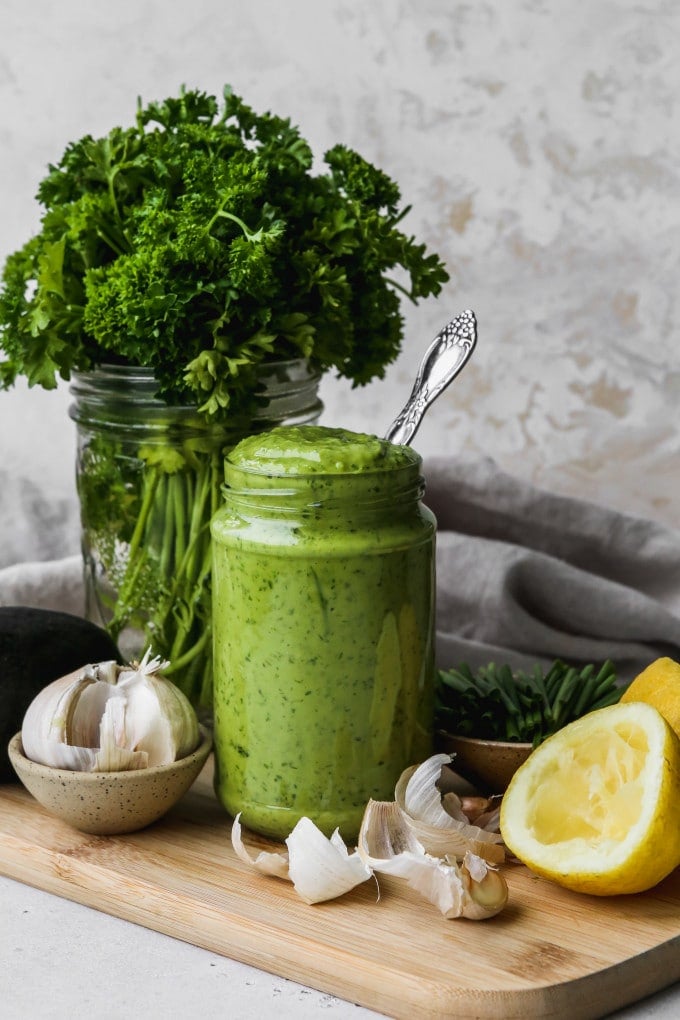 Straight on photo of a small glass jar filled with homemade avocado green goddess dressing.