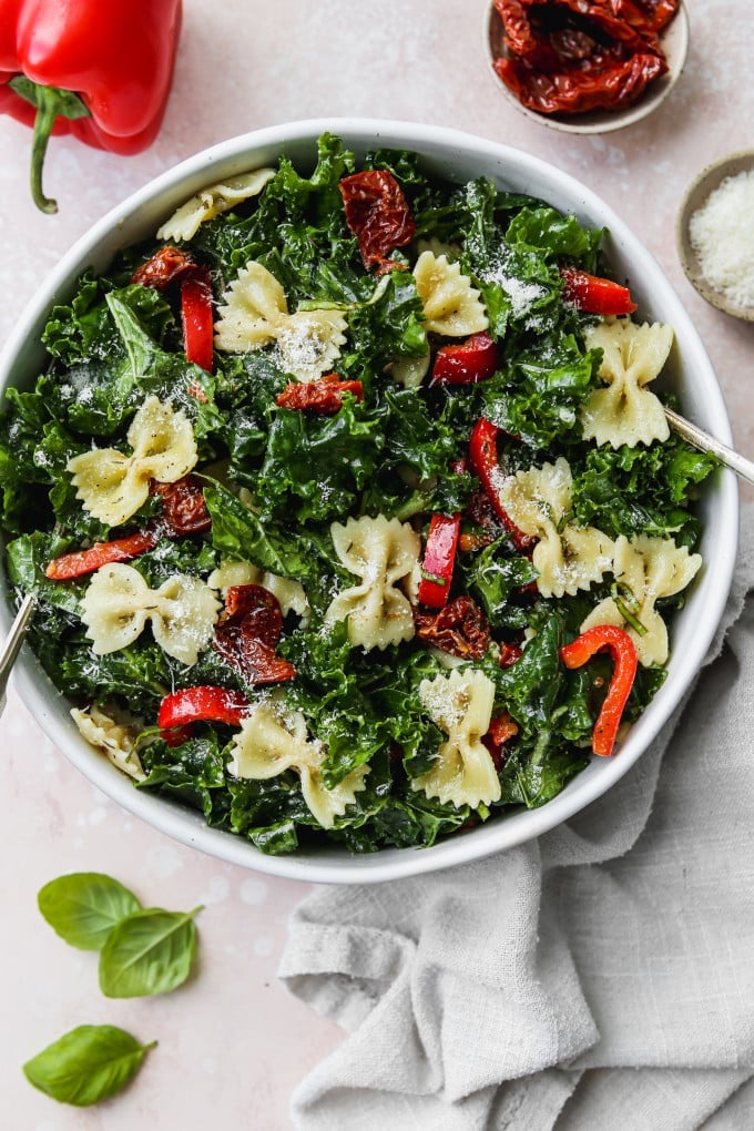 Overhead photo of a kale pasta salad with sundried tomatoes and peppers in a large white bowl.