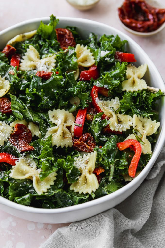 Closeup photo of a kale pasta salad with sundried tomatoes and peppers in a large white bowl.