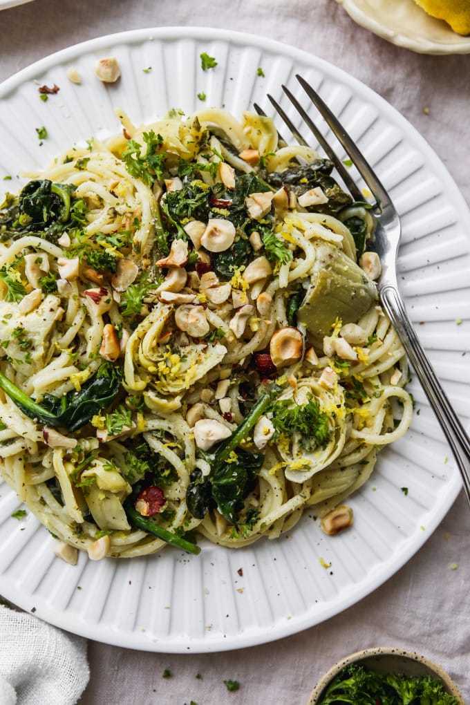 Closeup photo of a white plate topped with lemon artichoke and spinach pasta.