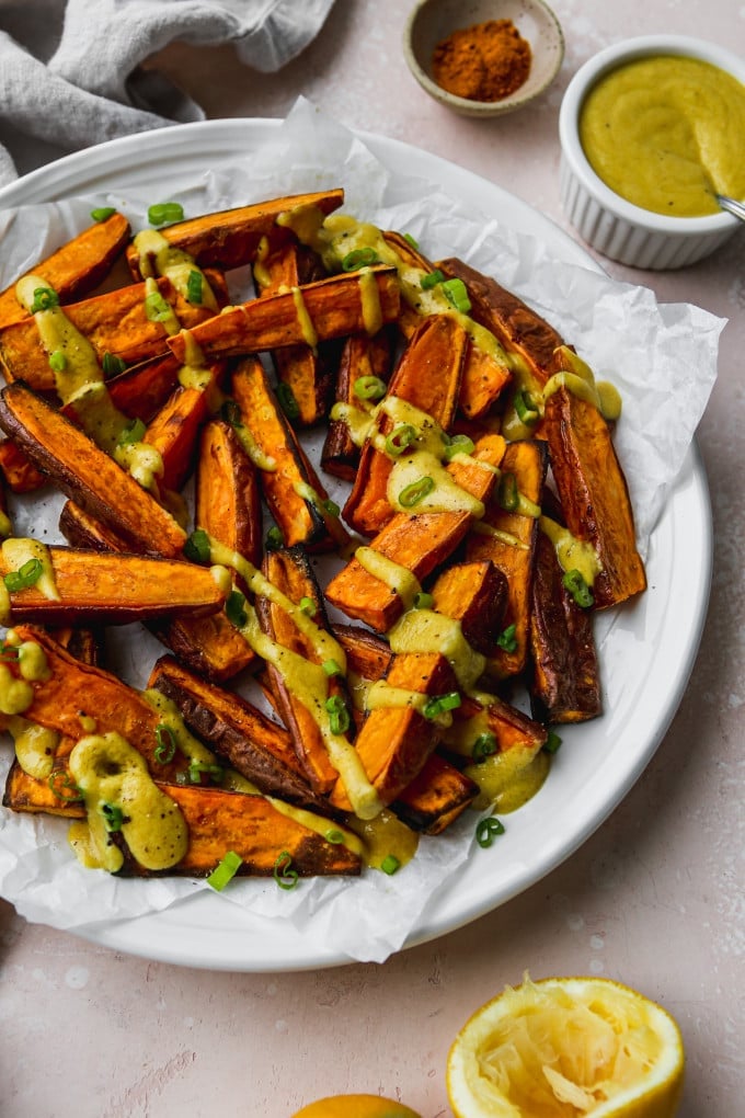 Overhead photo of roasted sweet potato wedges with curry tahini dressing drizzled on top.