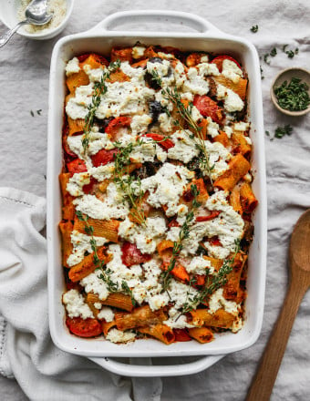 Overhead photo of an eggplant, zucchini, and tomato baked pasta topped with ricotta, parmesan and thyme in a baking dish.