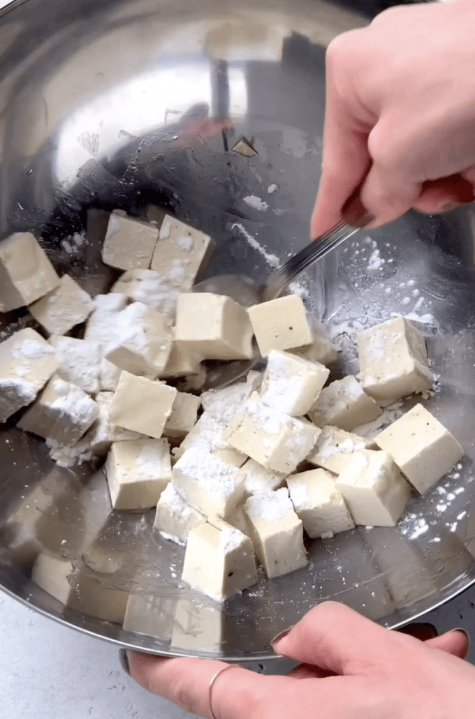 Tossing tofu cubes in cornstarch in a mixing bowl.