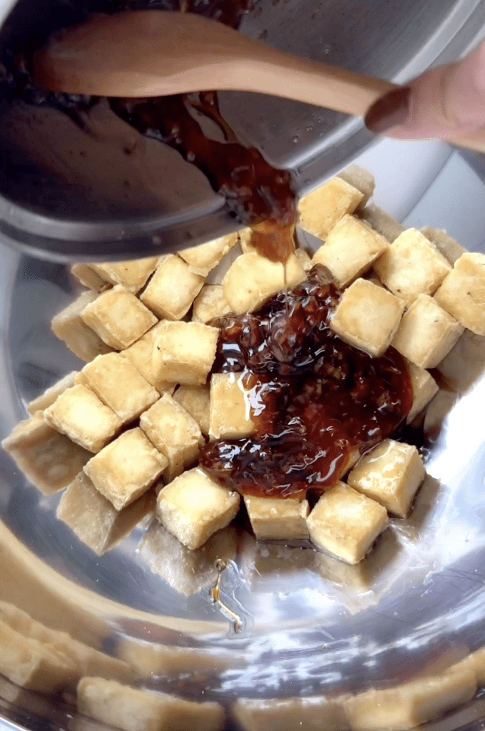 Pouring honey garlic sauce over baked tofu cubes.