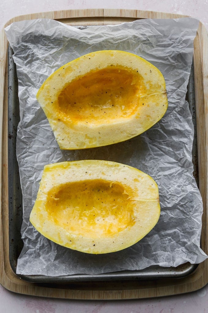 Overhead photo of halved spaghetti squash brushed with olive oil on baking sheet.