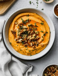 Overhead photo of pumpkin whipped feta in a bowl topped with walnuts, thyme, and honey.