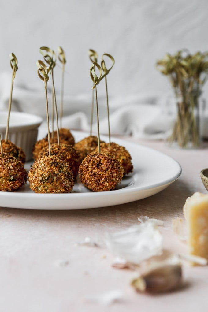 Straight on photo of parmesan crusted brussels sprouts bites on a white plate with skewers in them.
