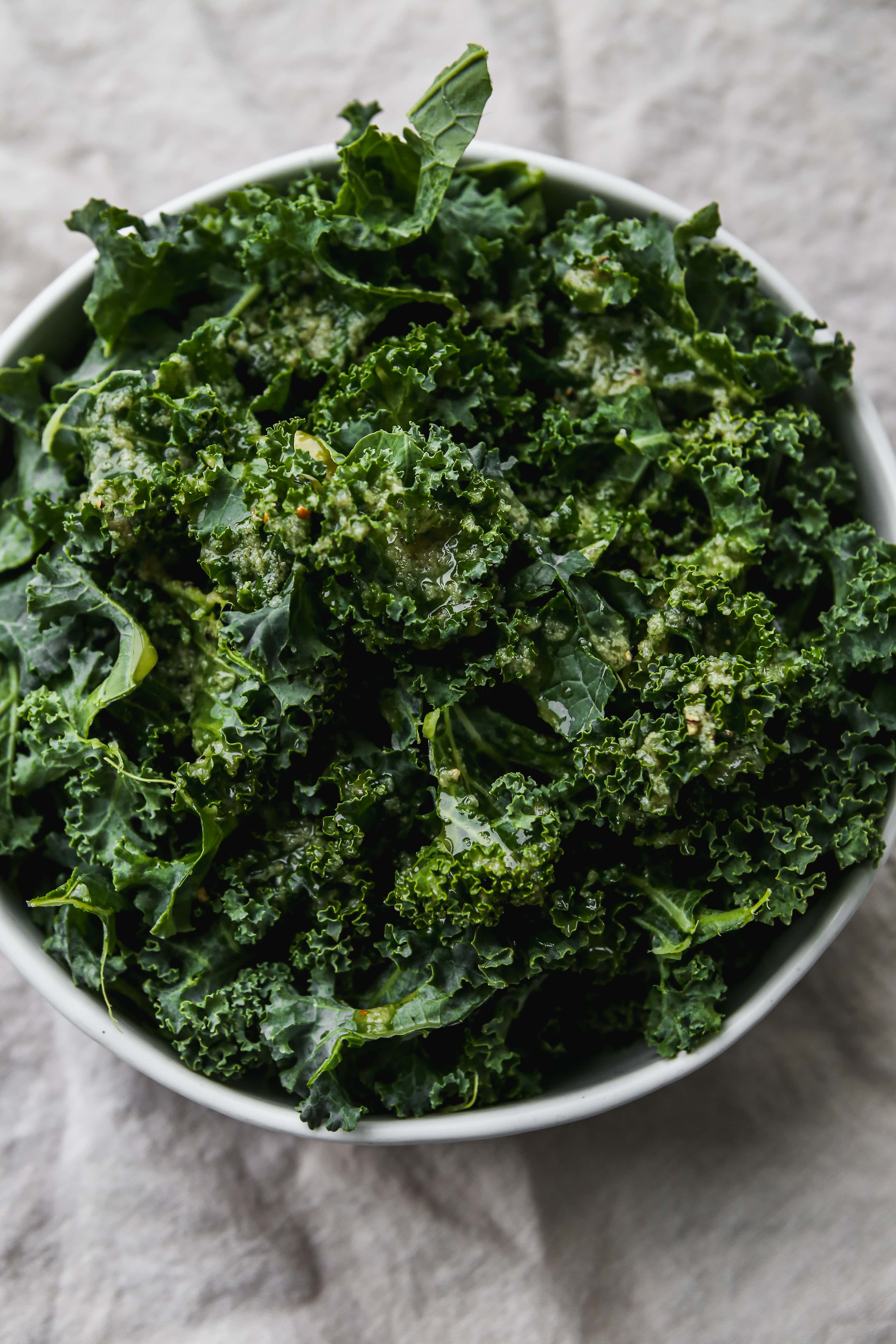 Overhead photo of a bowl of kale leaves with salad dressing overtop.