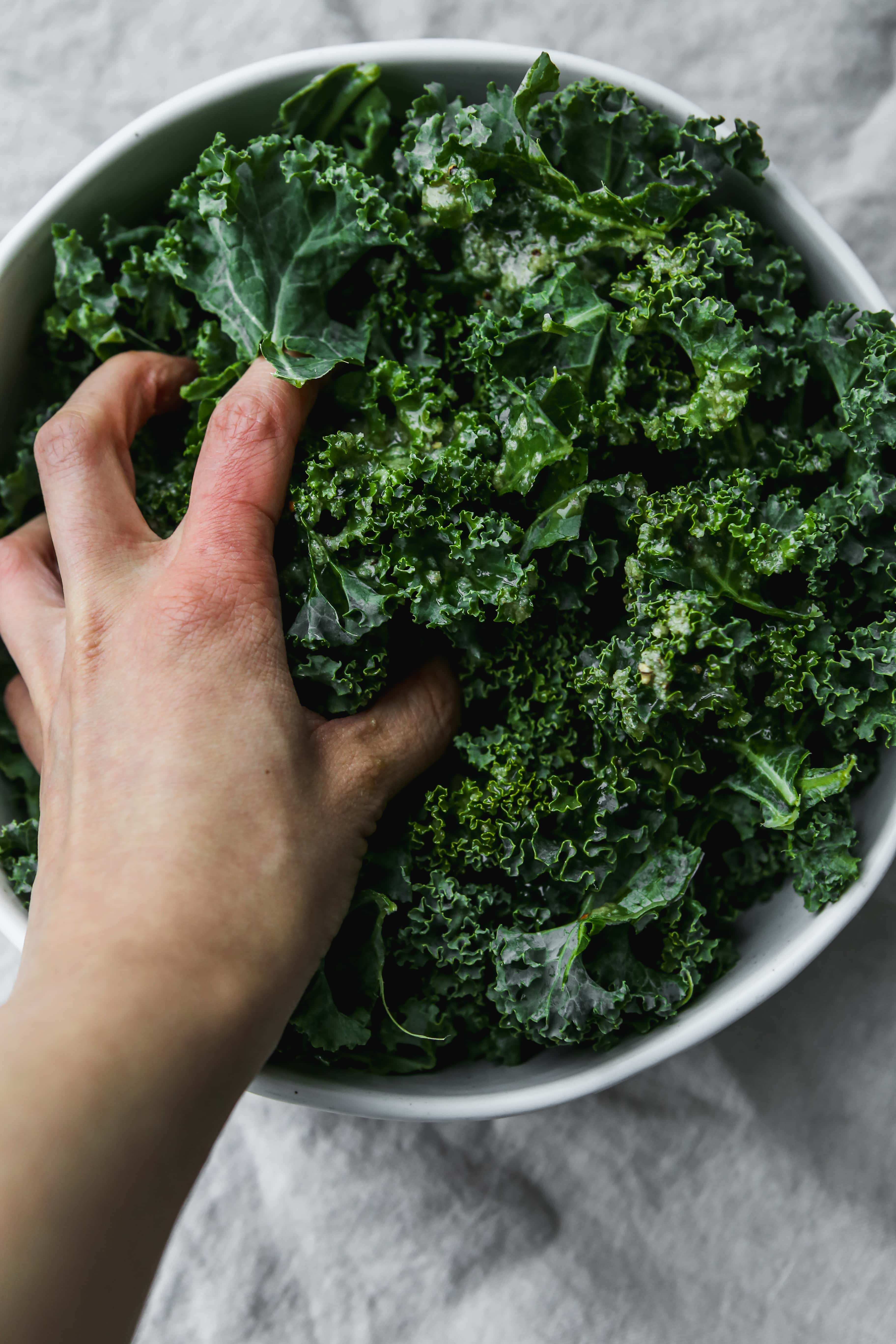 Overhead photo of a hand massaging kale leaves in a bowl.