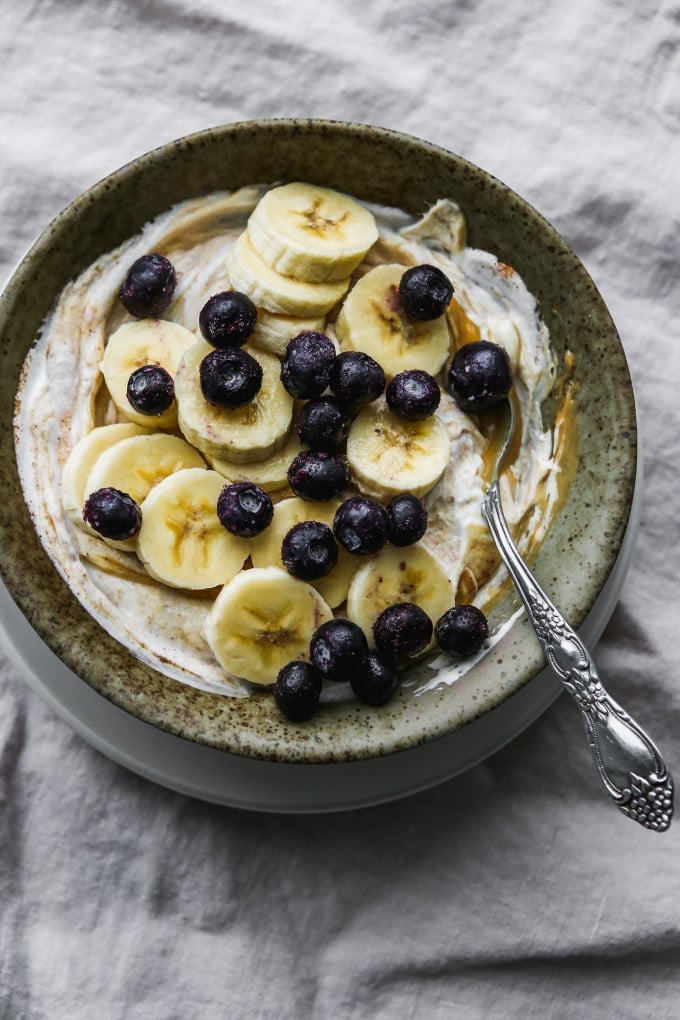 Overhead photo of a peanut butter greek yogurt bowl topped with bananas and blueberries.
